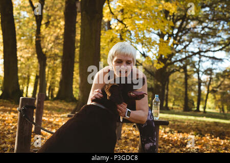 Donna Senior in un parco addensarsi il suo cane Foto Stock