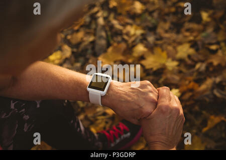 Senior donna utilizzando un orologio intelligente in un parco Foto Stock