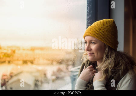 Donna che indossa il giallo beanie guardando fuori dalla finestra Foto Stock