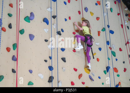 Un 7 anno vecchia ragazza si arrampica su una parete di arrampicata Foto Stock