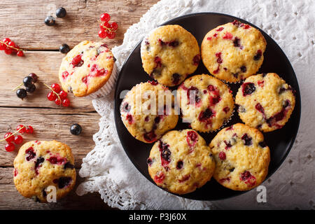 Muffin appena sfornati con il rosso e il nero bacche Ribes vicino sul tavolo. parte superiore orizzontale vista da sopra Foto Stock