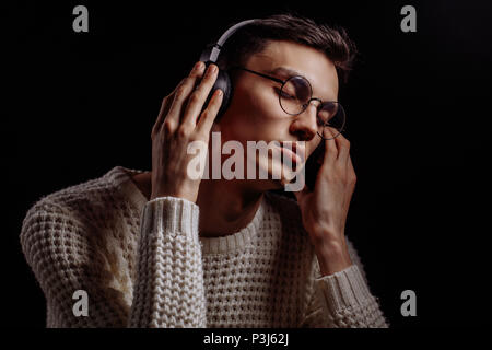 Giovane uomo che indossa gli occhiali e cuffie per ascoltare musica su  sfondo nero Foto stock - Alamy
