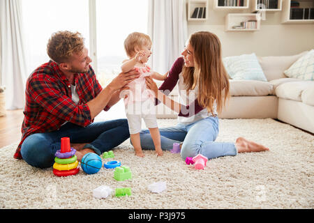 Coppia giovane aiutando toddler stand figlia in salotto Foto Stock