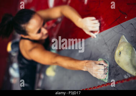 Bella giovane donna forte arrampicata su rosso parete artificiale vista dall'alto. Foto Stock