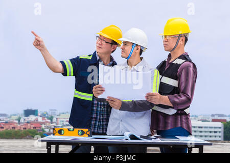 Asian tecnico delle costruzioni e i suoi capisquadra lavorando insieme e controllare i progressi compiuti a livello sito in costruzione, buona per il lavoro di squadra e tema di ingegneria Foto Stock