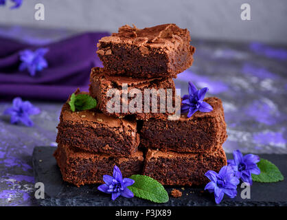 Pezzetti di cioccolato di brownie pie sono impilati su un nero grafite lastra decorata con fiori di colore blu Foto Stock