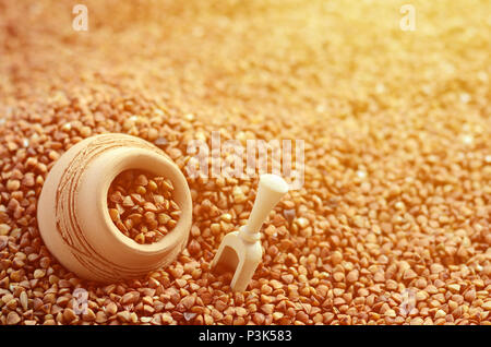 Immagine di sfondo di un gran mucchio di grano saraceno, al centro del quale si trova una piccola brocca e una spatola in legno per i cereali Foto Stock