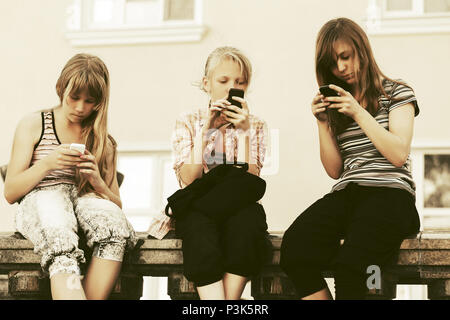 Un gruppo di ragazze adolescenti chiamata sui telefoni cellulari contro un edificio scolastico Foto Stock