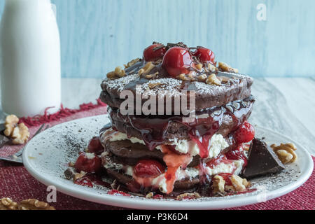 Deliziose frittelle di cioccolato - dessert gourmet per colazione? Primo piano di una pila di frittelle farcite con ciliegie, panna e noci. Varie angolazioni Foto Stock