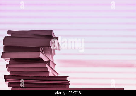 Pila di libri diversi, i libri di testo contro una luce rosa striato sfondo viola con copia spazio. Concetto di di cominciare la scuola, torna a scuola e istruzione Foto Stock