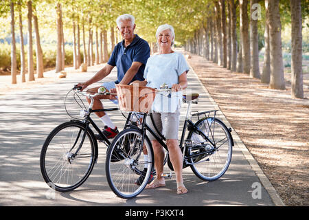Ritratto di sorridente coppia Senior ciclismo su strada di campagna Foto Stock