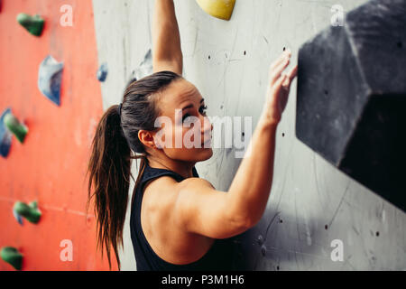 Bella giovane donna forte arrampicata su rosso parete artificiale vista dall'alto. Foto Stock