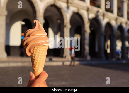 Mano che tiene un due-tono Soft servire il gelato cono, con sfocate in stile neoclassico edificio in background Foto Stock