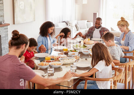 Due famiglie di pregare prima di gustare pasti a casa insieme Foto Stock