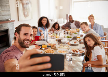 Due famiglie tenendo Selfie come essi godono di pasto a casa insieme Foto Stock