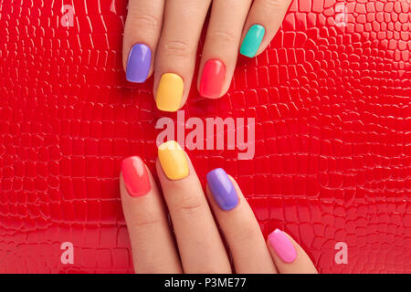 Manicure multicolore e laccato rosso sfondo. Foto Stock