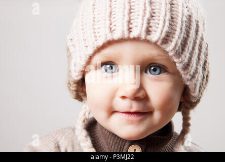 Ritratto di un simpatico baby girl in un enorme marrone berretto lavorato a maglia. Isolato su sfondo bianco. Foto Stock