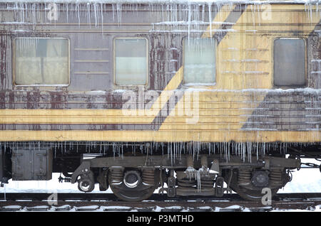 Foto dettagliate di una vettura congelate di treni passeggeri con ghiaccioli e ghiaccio sulla sua superficie. Stazione ferroviaria nella fredda stagione invernale Foto Stock