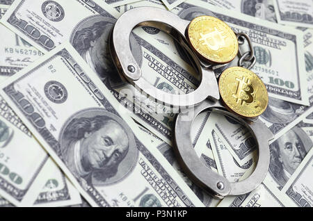 Polizia e manette bitcoins giacciono su un gran numero di fatture del dollaro. Il concetto di problemi con la legge durante il cryptocurrency illegale e di data mining Foto Stock