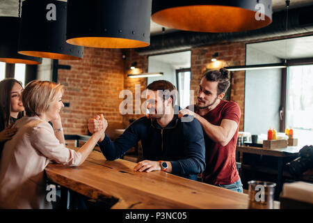 Allegro gyu e ragazza divertirsi wrestling braccio di ogni altro nel pub. Foto Stock