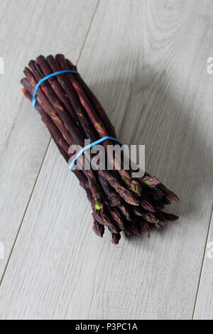 Mazzetto di asparagi viola legati insieme con fasce elastiche su un grigio Sfondo di legno Foto Stock