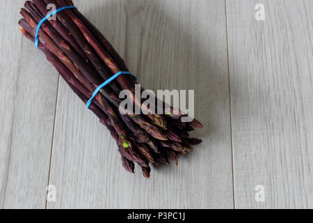 Mazzetto di asparagi viola legati insieme con fasce elastiche su un grigio Sfondo di legno Foto Stock