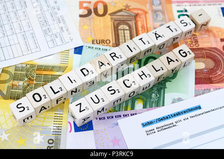 Lettera cube forma la parola solidarietà con supplemento sul denaro, Buchstabenwürfel formen das Wort Solidaritätszuschlag auf Geldscheinen Foto Stock