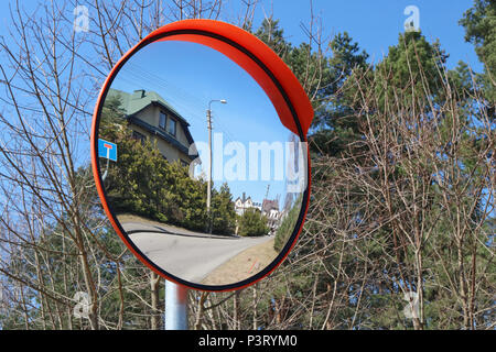 Un round specchio convesso è installato presso il villaggio crocevia per la sicurezza. Soleggiata giornata di primavera paesaggio Foto Stock