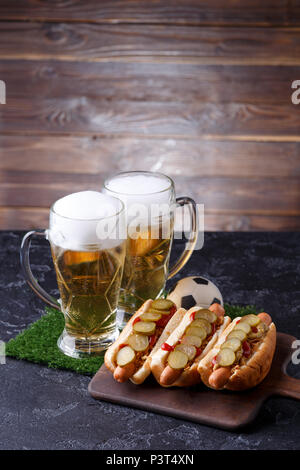 Foto di due bicchieri di birra, hot dogs, pallone da calcio Foto Stock