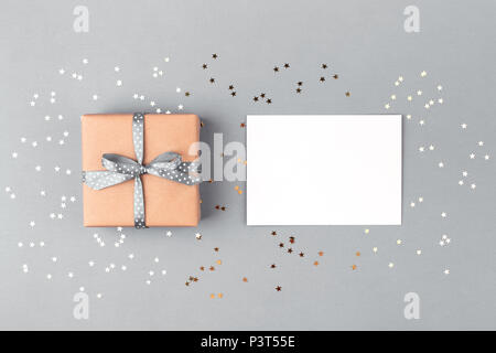 Confezione regalo avvolti in carta kraft e legate con nastro grigio e bianco bianco su sfondo grigio decorato con coriandoli. Vista dall'alto, il concetto di vacanza. Foto Stock