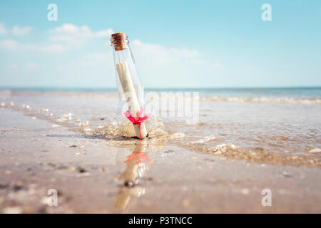 Un messaggio in bottiglia lavato fino a una spiaggia concetto per aiutare, sos di emergenza e assistenza Foto Stock
