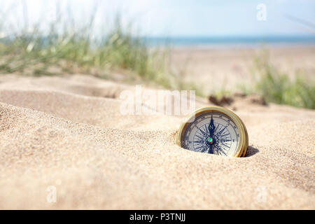 Golden Compass sepolto nella sabbia sulla spiaggia concetto per la perdita o la direzione Foto Stock