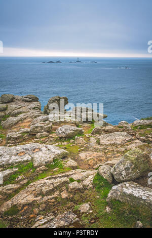 Grandi massi sulla costa e piccolo faro sullo sfondo di Lands End - raggiungere il punto più a ovest dell'Inghilterra che è una meta turistica molto a Foto Stock