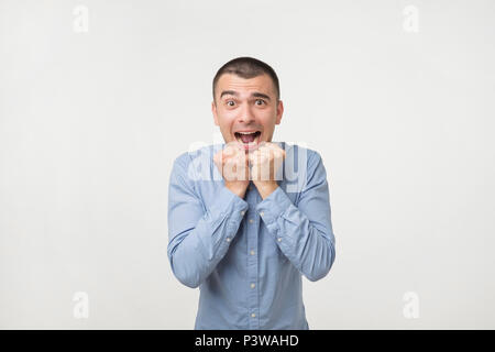 Giovane bella uomo isolato su sfondo grigio. Concetto di celebrando la vittoria tenendo i pugni in profonda espressione emotiva di felicità. Studio sho Foto Stock