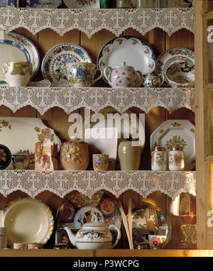 Colose di vintage piatti di porcellana cinese e teiere su scaffali di pino con bordo in pizzo Foto Stock