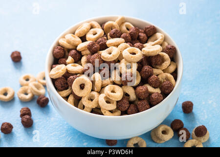 Una sana colazione di cereali sul blu. Le sfere di cioccolato e anelli di mais in bianco ciotola. Close up. Foto Stock