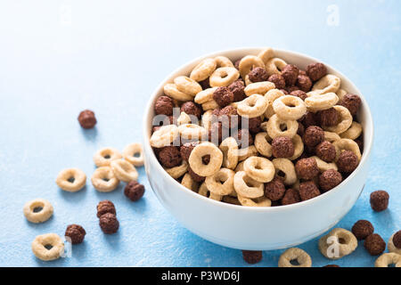 Una sana colazione di cereali sul blu. Le sfere di cioccolato e anelli di mais in bianco ciotola. Foto Stock