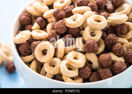 Una sana colazione di cereali sul blu. Le sfere di cioccolato e anelli di mais in bianco ciotola. Close up. Foto Stock