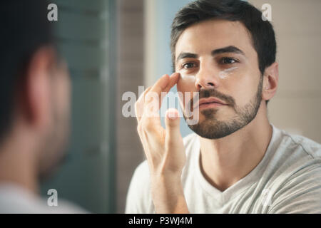 Giovane uomo applicazione anti-invecchiamento fot lozione per la cura della pelle Foto Stock