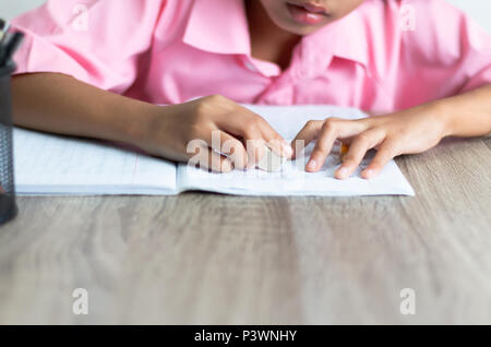 I bambini utilizzano un eraser è eliminazione di parole. Chiudere la bambina sta facendo i compiti sul tavolo di legno. Selezionare la messa a fuoco la profondità di campo di una copia con Foto Stock