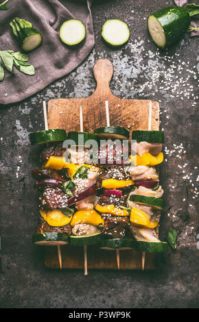 Varie spiedini di carne di pollo e carne di manzo sul tagliere su sfondo scuro con verdure. Preparazione Grill, vista dall'alto Foto Stock