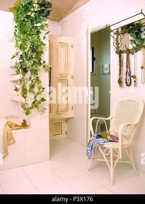 Trailing pianta verde sulla parete sopra il bagno in vecchio stile bagno con il bastone bianco sedia Foto Stock