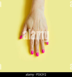 Mano femmina con unghie rosa su giallo. Concetto. Foto Stock