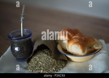 Mate argentino com saco de erva (Ilex paraguariensis) e prato Medialunas com. Foto Stock