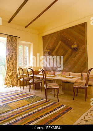 Tappeto a motivi geometrici e patchwork da parete nella sala da pranzo con alto soffitto a travi e montato posti a sedere al tavolo lungo Foto Stock