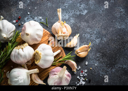 Spicchi di aglio con le spezie e le erbe su una pietra scura sullo sfondo. Vista superiore, copia dello spazio. Foto Stock