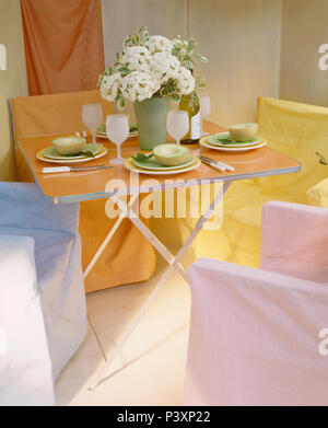 Pastel loose-copre il direttore di sedie intorno al tavolo pieghevole fissato per il pranzo in economia in stile sala da pranzo Foto Stock