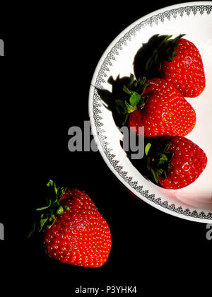 Fragole rosso in una piastra bianca su sfondo nero Foto Stock