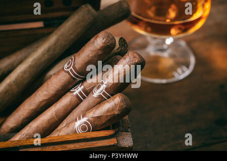 Sigari cubani in una scatola di legno, blur bicchiere di brandy Cognac, closeup vista con dettagli, spazio di copia Foto Stock