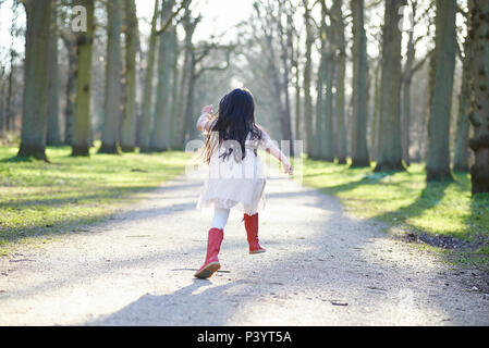 Carino ragazza asiatica in un abito bianco che corre lungo un percorso in prospettiva in un parco bellissimo sole primaverile Foto Stock